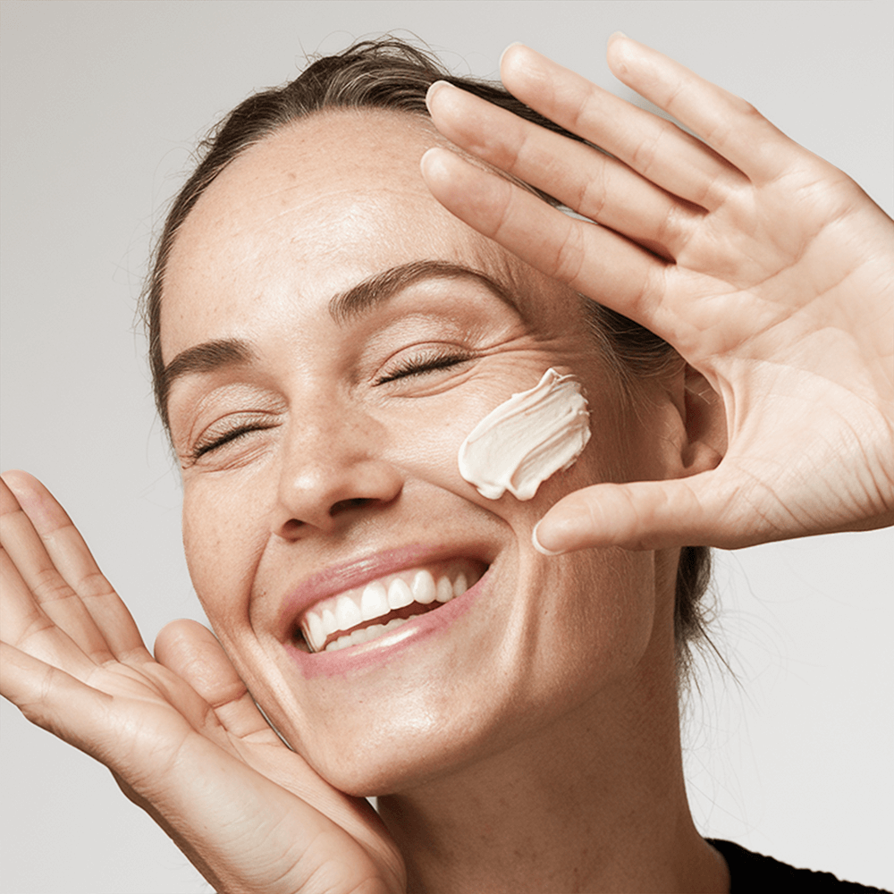 Woman applying cream as part of a natural skincare for women over 35 routine with a joyful expression