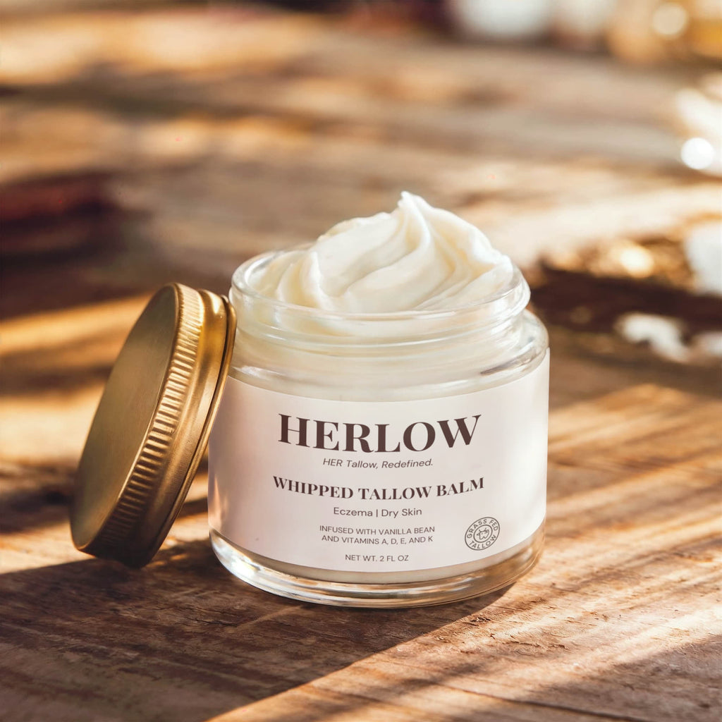 HERLOW grass-fed tallow balm in a glass jar with gold lid on wooden surface