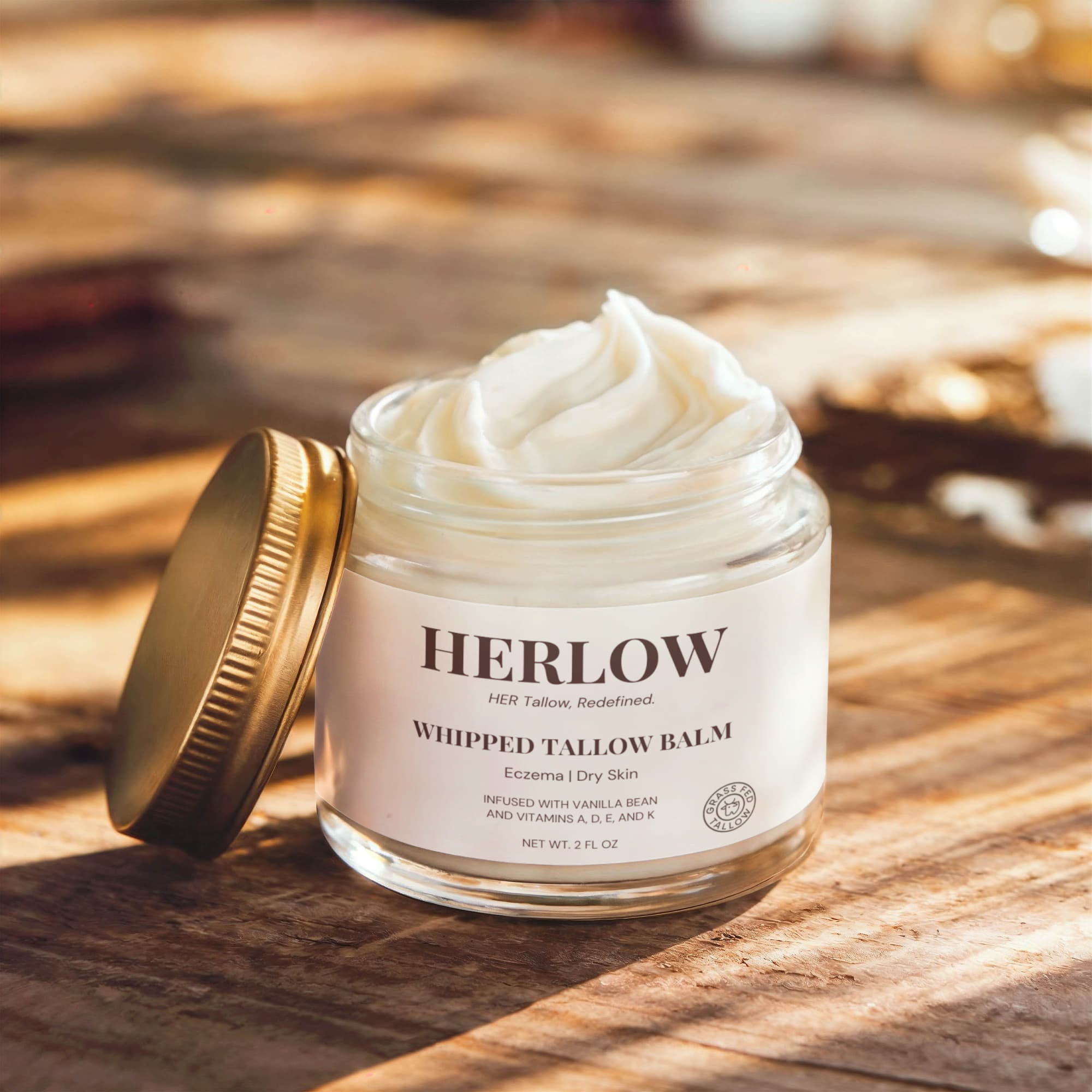 HERLOW grass-fed tallow balm in a glass jar with gold lid on wooden surface