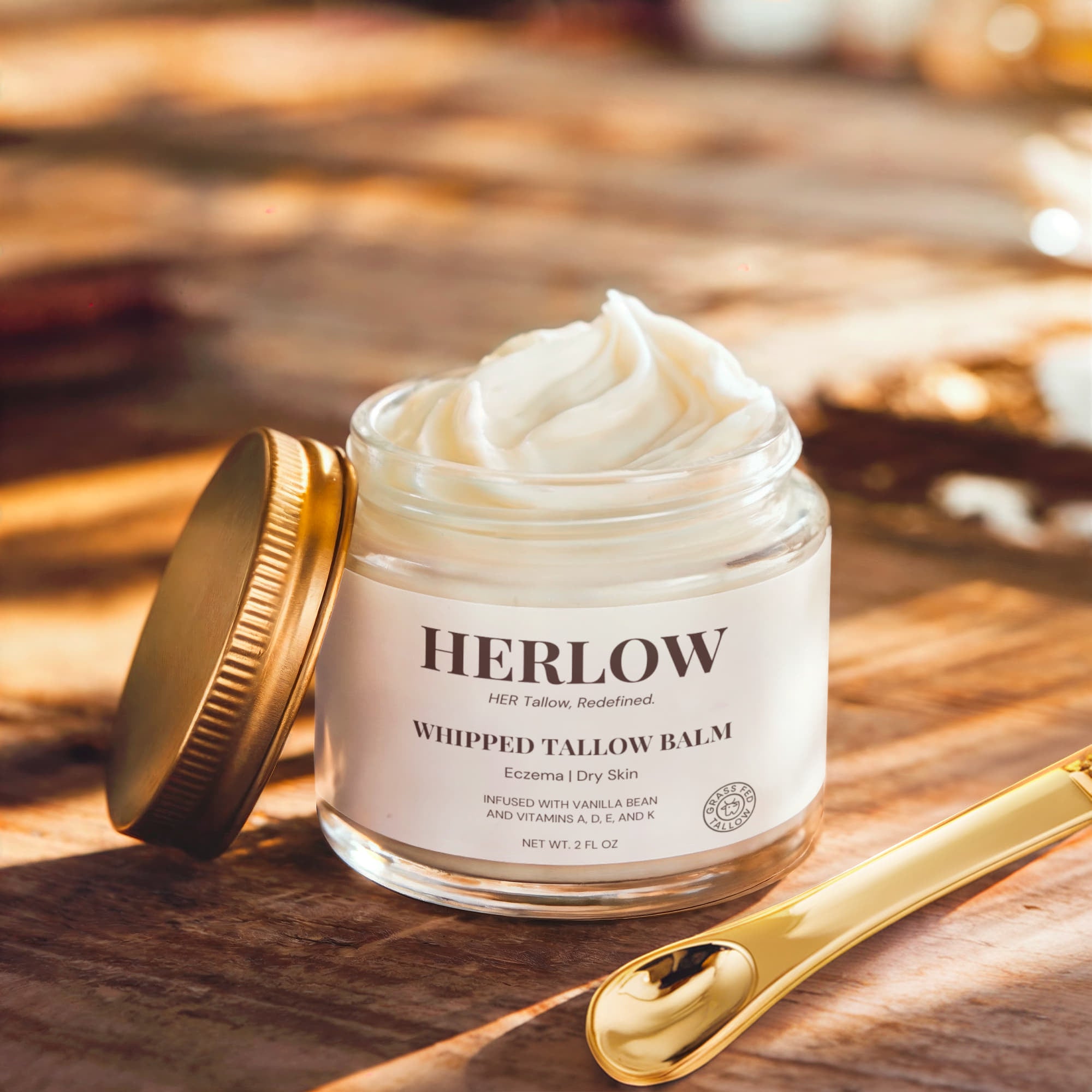 HERLOW whipped tallow balm in glass jar with gold lid and spoon on wooden surface grass-fed tallow balm
