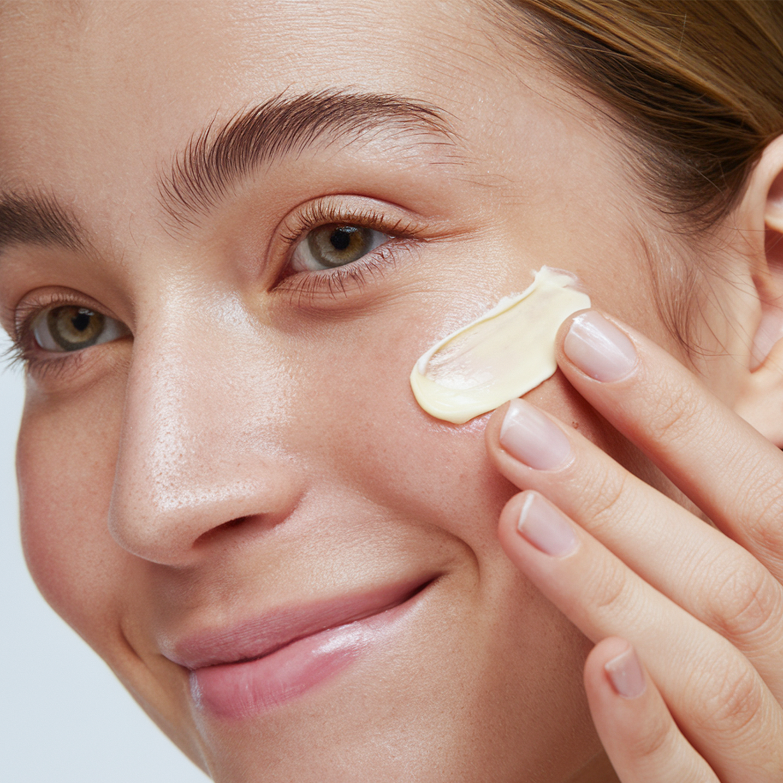 Woman applying HERLOW pro-aging face cream to her cheek for healthy, youthful skin